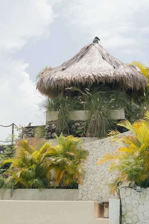 Free A rustic straw hut located on a tropical hillside, enveloped by lush greenery and blue skies. Stock Photo