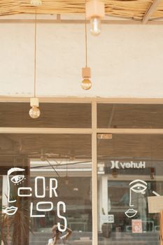 A stylish shopfront with unique glass panel art and hanging bulbs, reflecting urban street life.