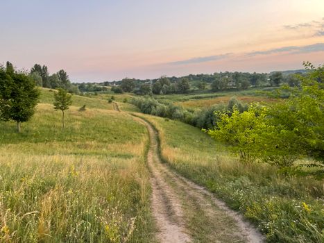 A serene countryside path through lush fields under a pastel sunset sky.