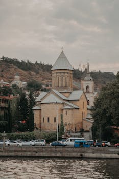 Historical cathedral in Tbilisi, Georgia with parked cars along the roadside.