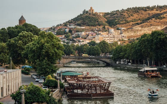Picturesque view of Tbilisi with river and hills, featuring iconic landmarks and vibrant surroundings.