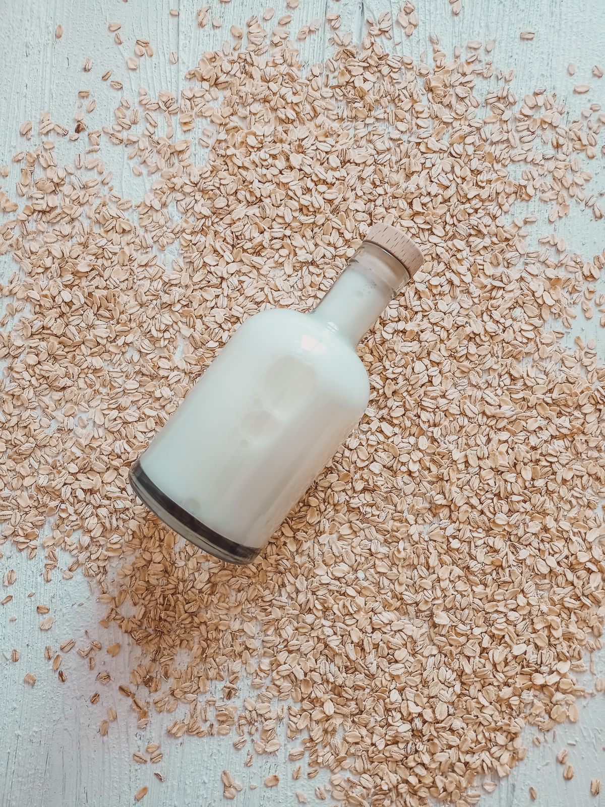 Unbranded glass bottle of oat milk resting on whole oats