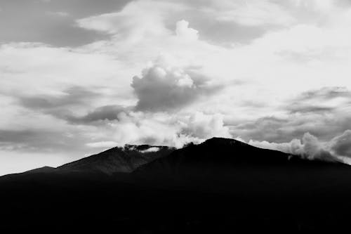 Grayscale Photo of Mountains Under Cloudy Sky