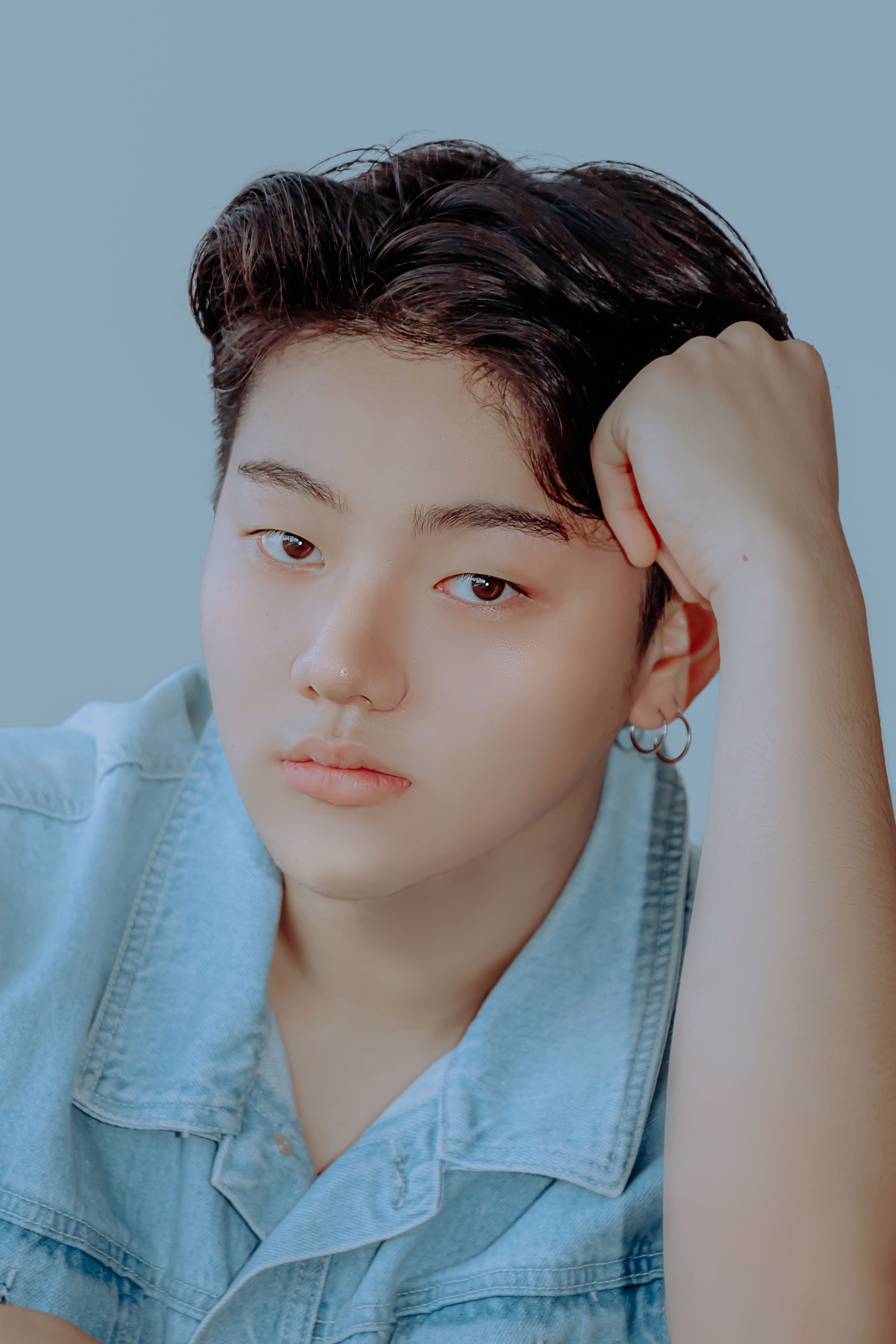 A serene and contemplative portrait of an East Asian man with a hand on his head wearing denim jacket.