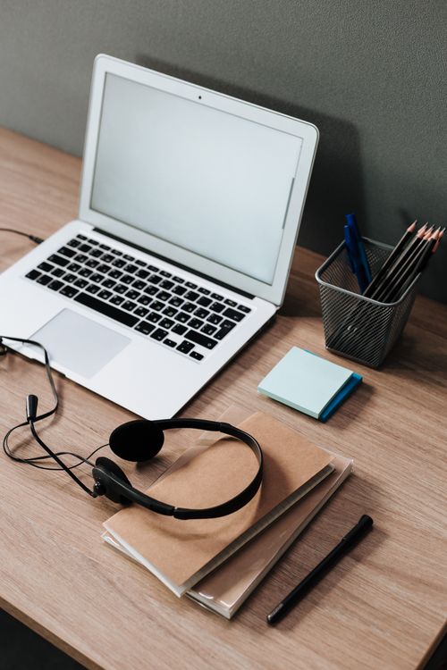 Free A clean and organized work desk setup featuring a laptop, headset, notebooks, and stationery essentials. Stock Photo