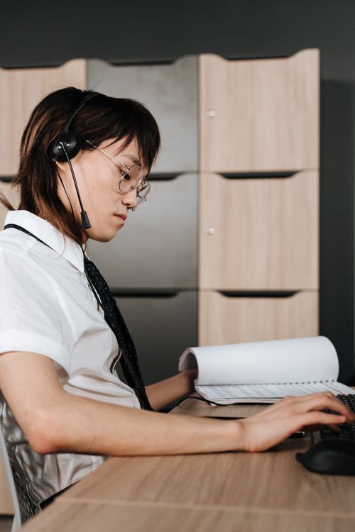 Free Call center agent wearing a headset, intently working on a computer in an office. Stock Photo