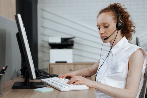 Free A female call center agent typing on a keyboard while wearing a headset at her desk. Stock Photo