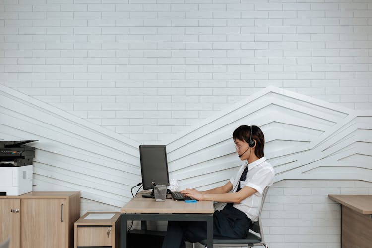 A Woman In White Polo Shirt Sitting On Chair Using A Computer