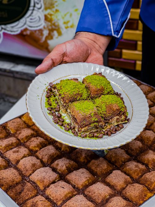 Free Freshly made pistachio baklava held on a decorative plate over more desserts. Stock Photo