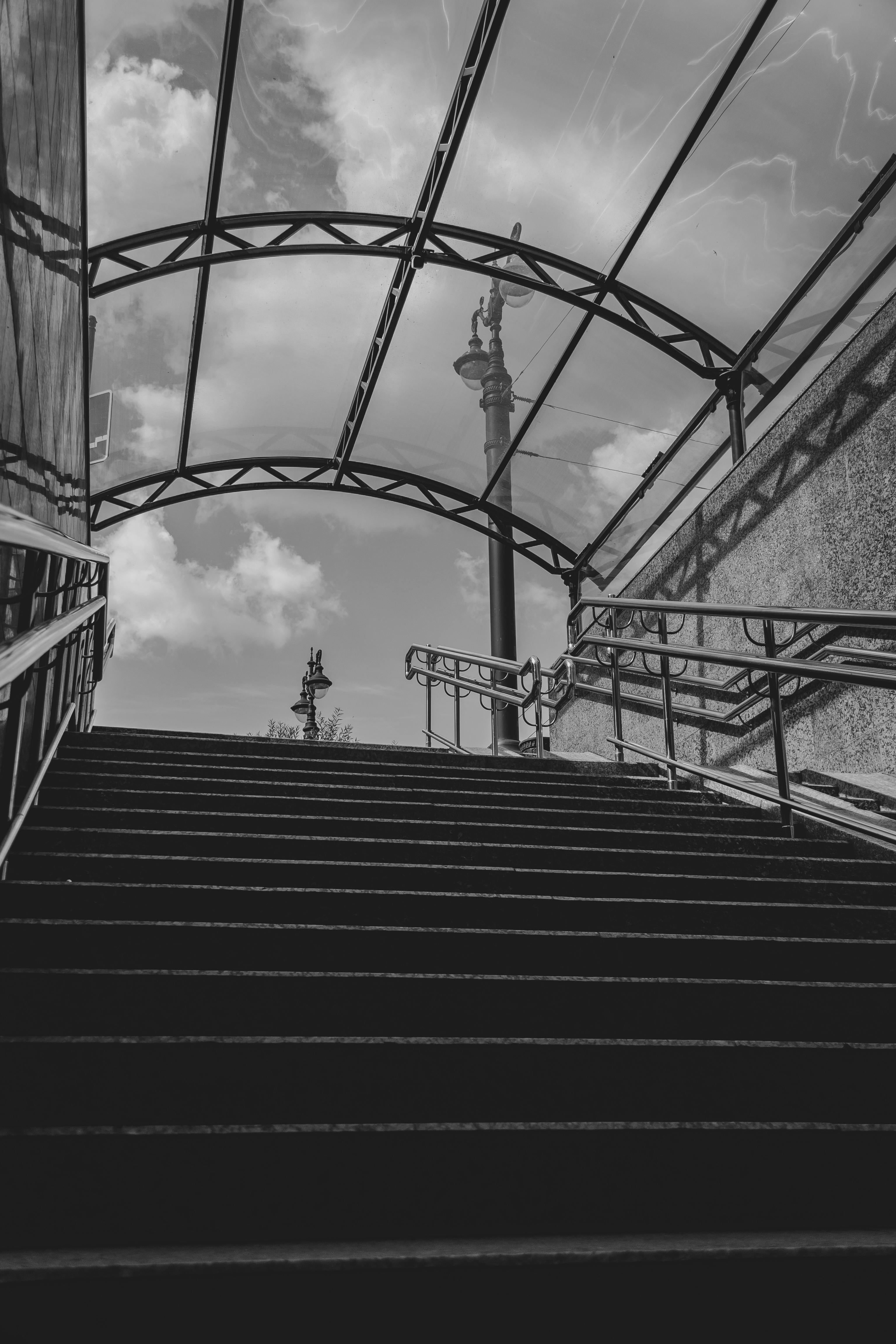 Monochrome image of a staircase leading to an open sky view with decorative metal frame.