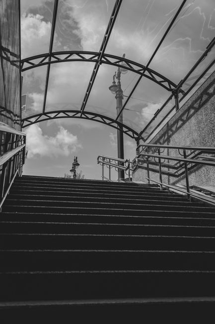 Monochrome image of a staircase leading to an open sky view with decorative metal frame.