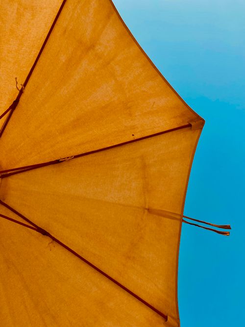 Free A yellow umbrella provides a striking contrast against a clear blue summer sky. Stock Photo