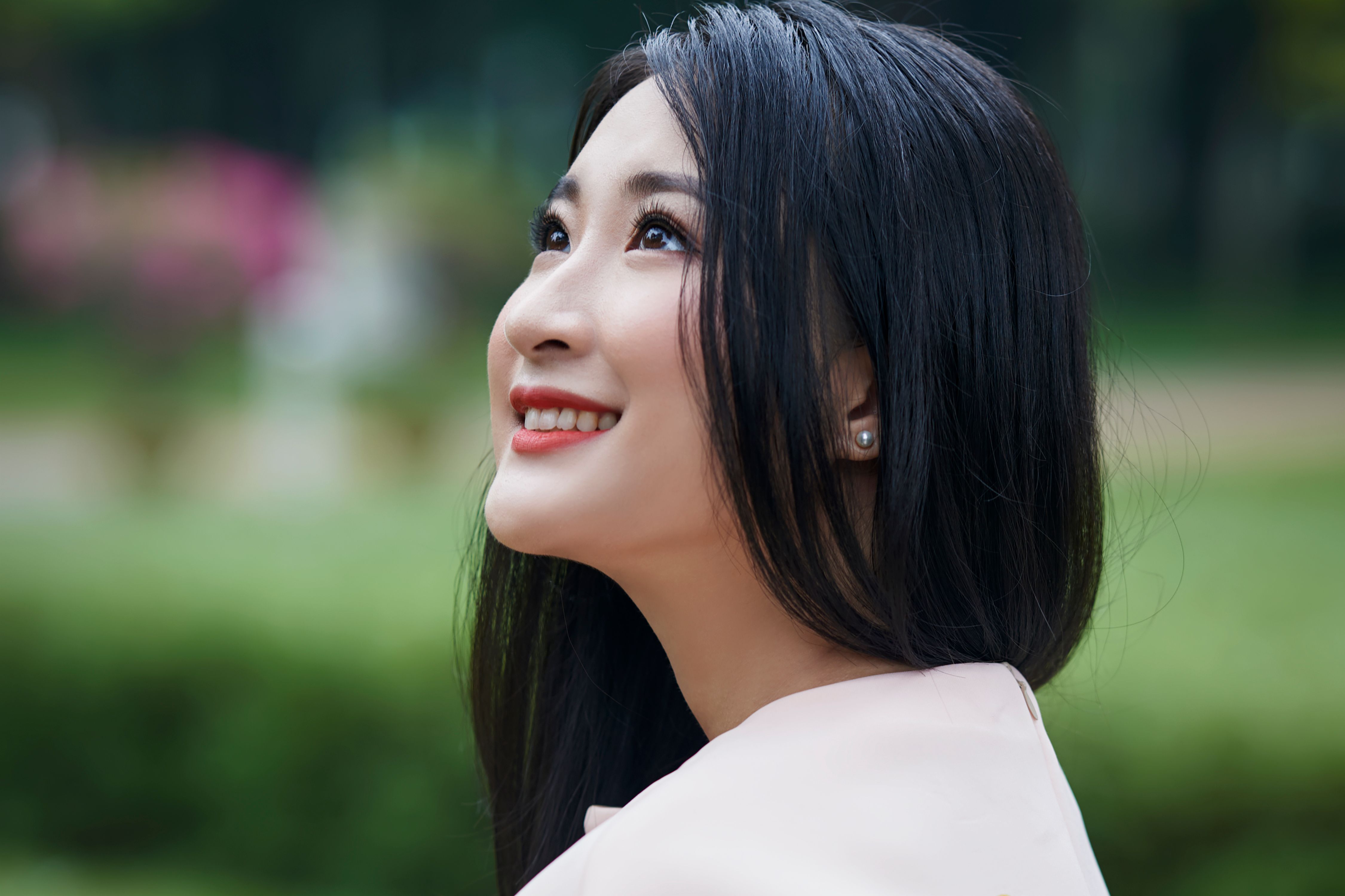 Portrait of a smiling Asian woman looking up, enjoying nature outdoors.
