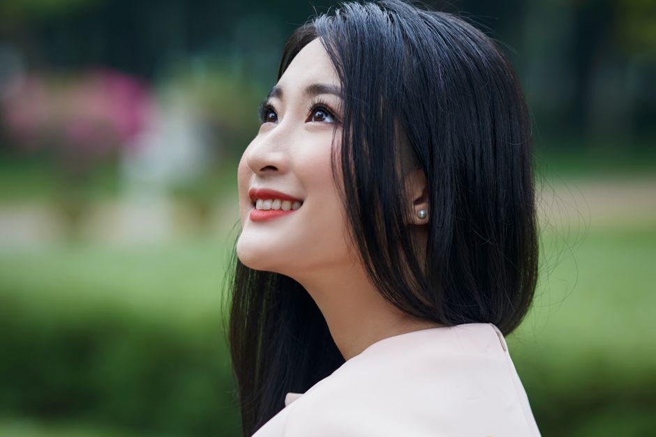 Portrait of a smiling Asian woman looking up, enjoying nature outdoors.