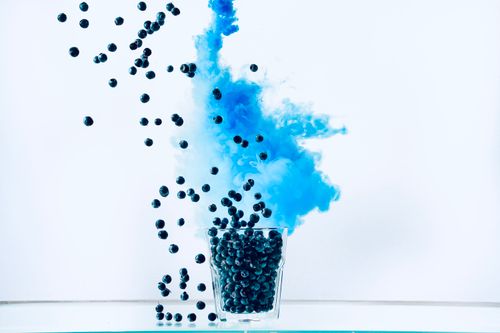 Free Dynamic image of blueberries falling into a glass with blue smoke on a white background for an artistic effect. Stock Photo