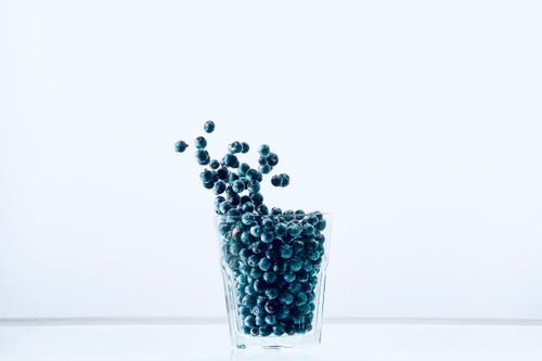 Free Fresh blueberries spilling from a glass on a minimalist white background. Perfect for food and health themes. Stock Photo