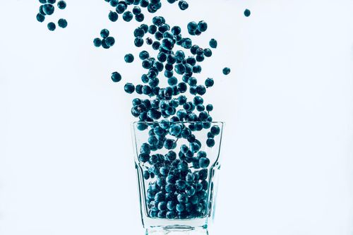Free Blueberries falling into a clear glass against a white background, capturing freshness and simplicity. Stock Photo