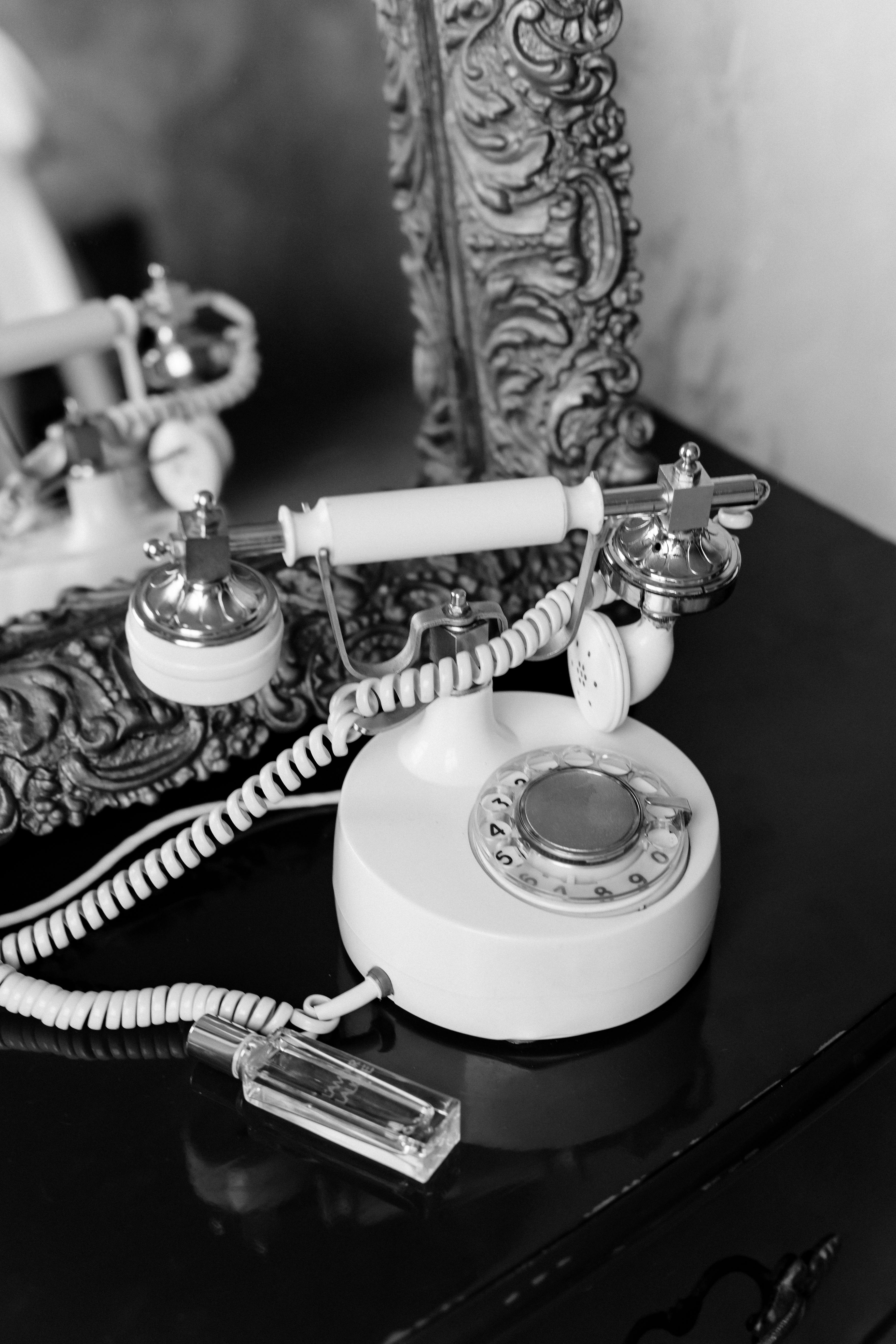Black and white photo of a vintage rotary phone with a baroque frame reflection.