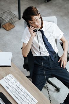 Asian call center agent on phone in an office, sitting at a desk with computer.