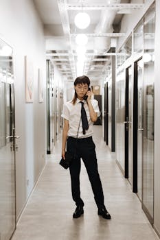 Asian professional in a modern office hallway talking on the phone, conveying a business environment.