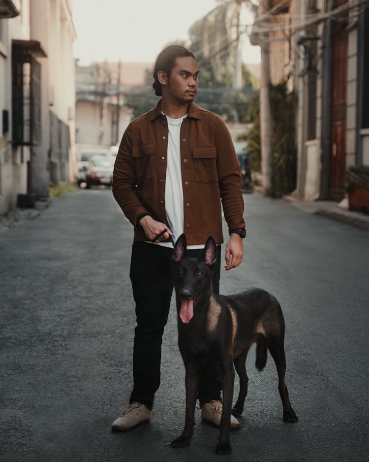 Man Wearing A Brown Jacket Holding A Black Dog