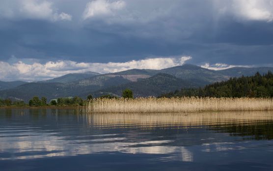 Calm lake view with mountain backdrop and cloudy sky, perfect for nature lovers.