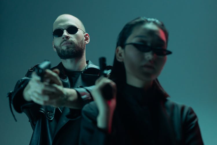 A Man And A Woman Holding A Gun While Looking At The Camera