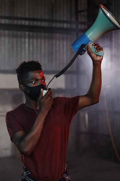 Free African American man holding a megaphone and wearing a face mask indoors during the pandemic. Stock Photo