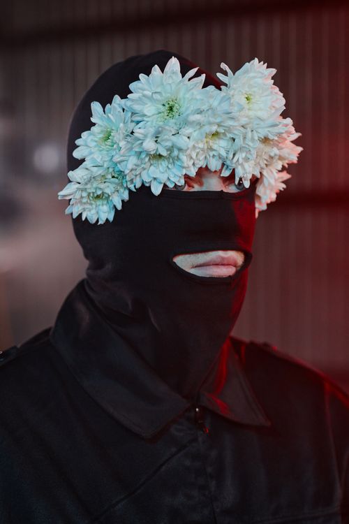 Free Dramatic portrait featuring a person in a balaclava adorned with white flowers against a moody backdrop. Stock Photo
