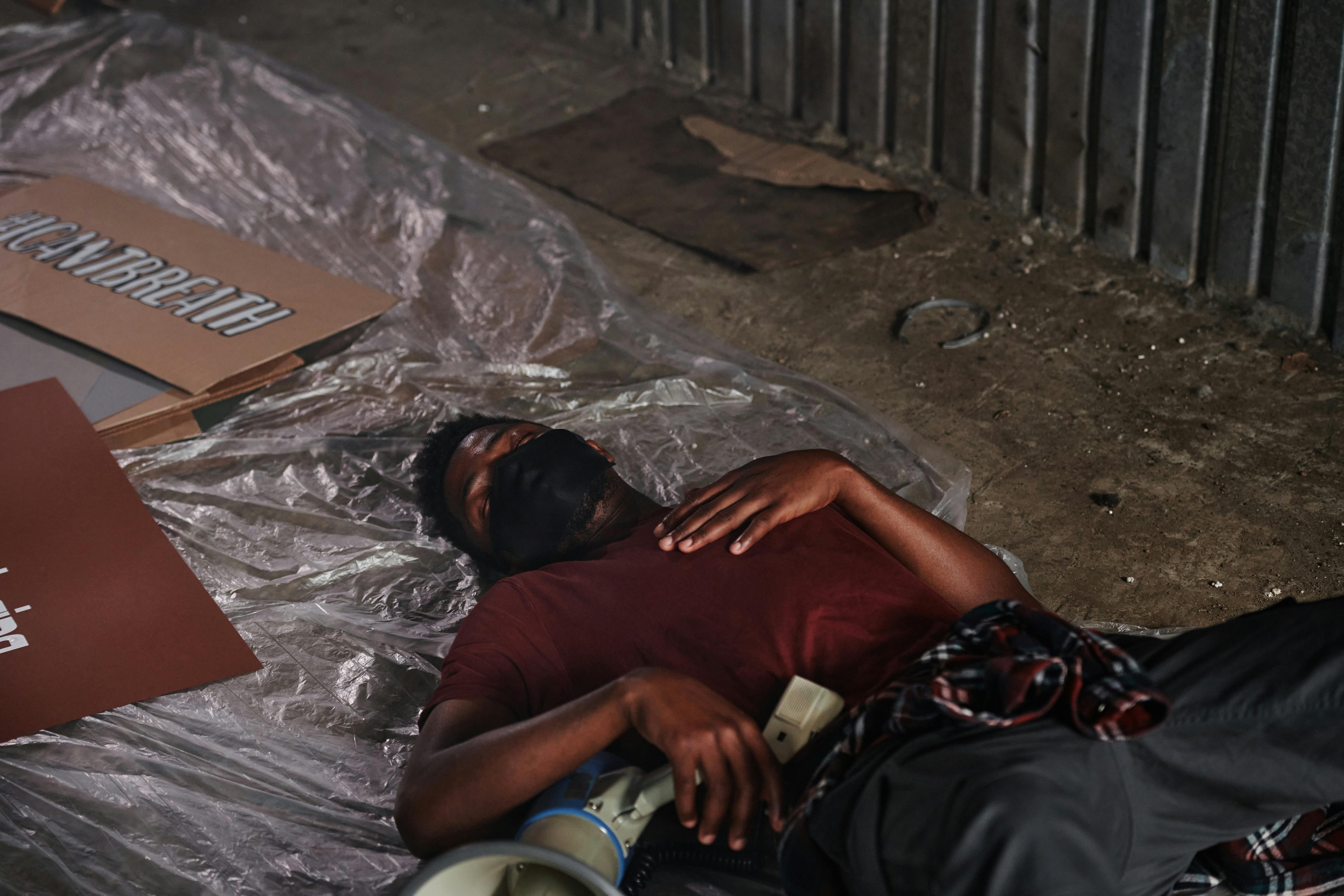 A Man in Red Shirt Wearing Face Mask while Sleeping on the Ground