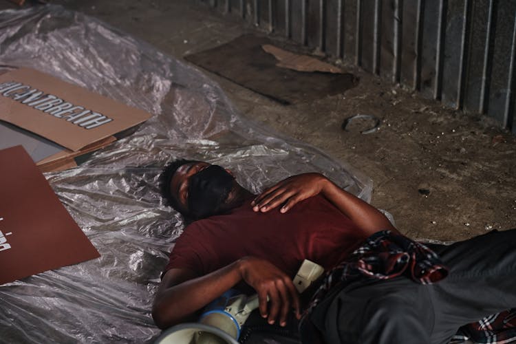 A Man In Red Shirt Wearing Face Mask While Sleeping On The Ground