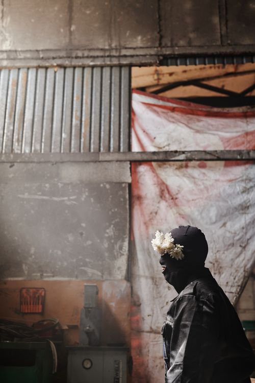 Free Moody portrait of a person wearing a balaclava with flowers in an industrial setting. Stock Photo