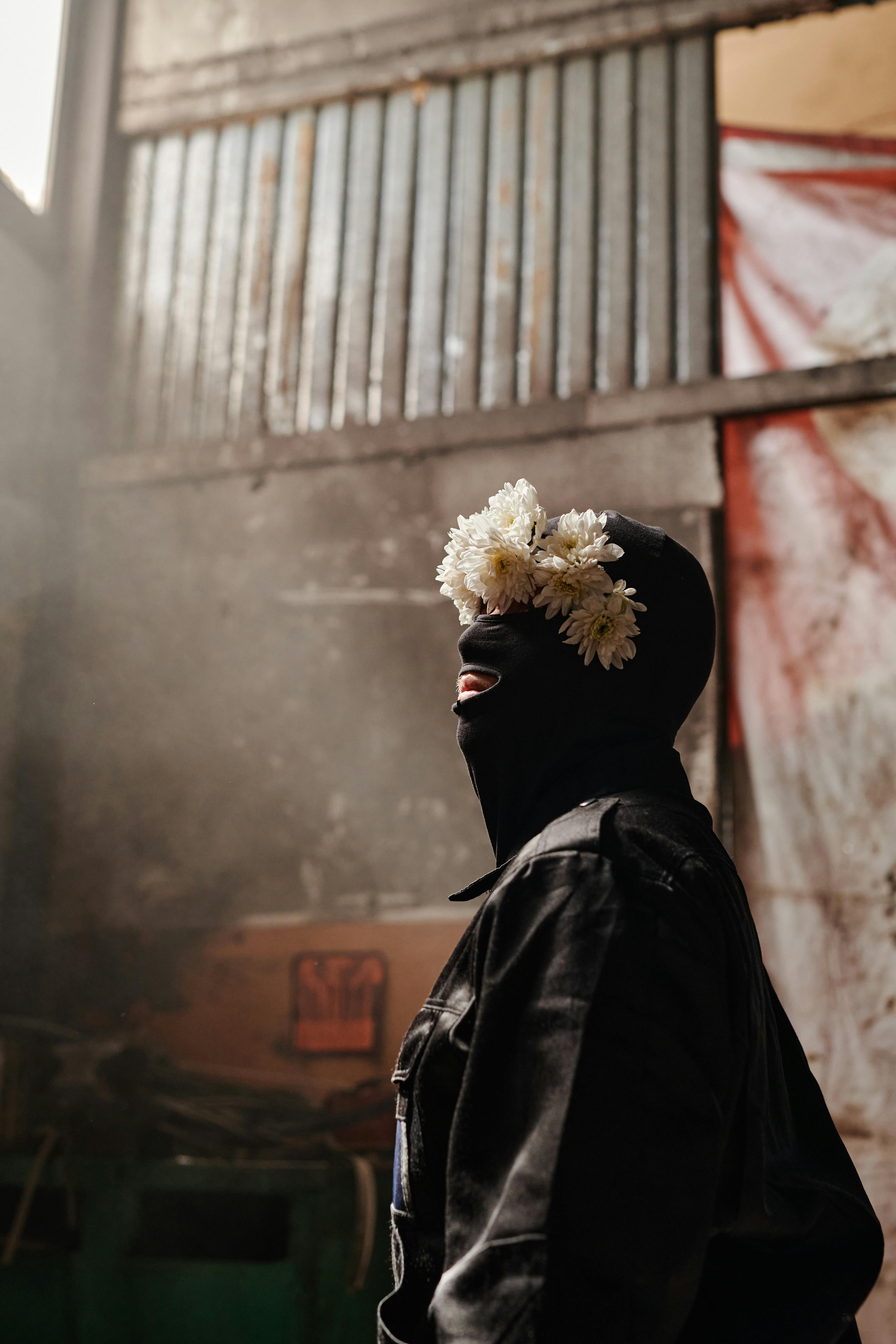 A striking portrait of a person in a balaclava adorned with flower headband, gazing upwards.
