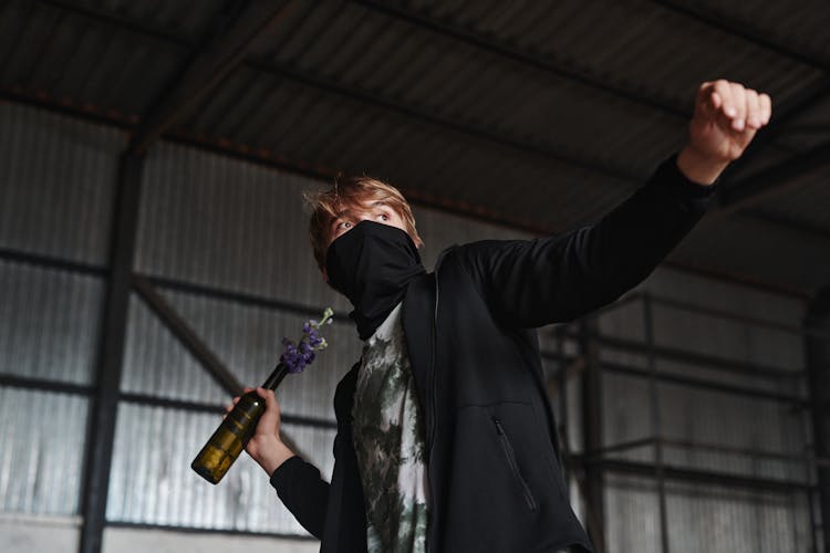 Man With A Mask Throwing A Bottle With Flowers