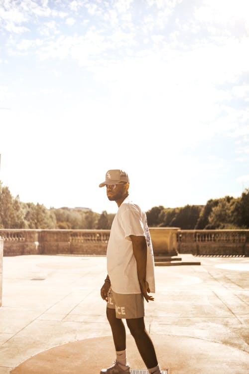 A Man in White Shirt and Cap Standing on an Open Ground while Posing at the Camera