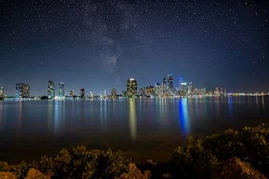Breathtaking view of Miami's skyline at night with a star-filled sky reflecting over the water.