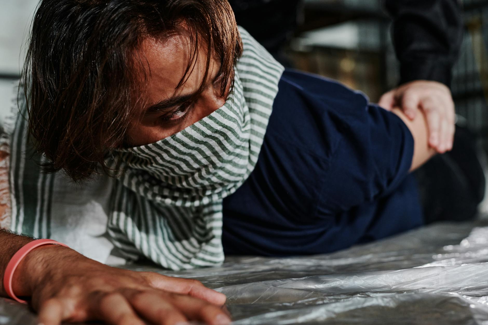Close-up of a man on the ground wearing a scarf, being restrained by another person.