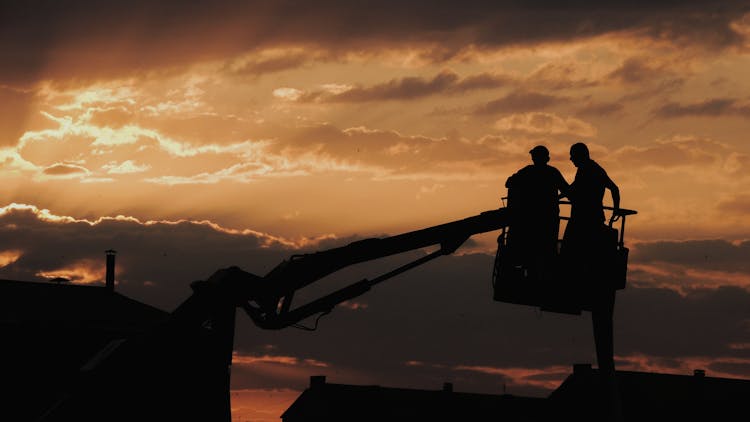 Silhouette Of People On Construction Crane Arm