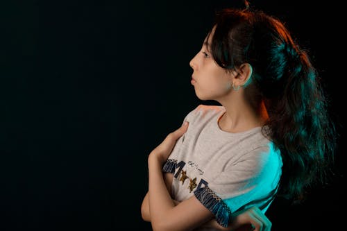 Woman in Gray Shirt Standing Near Black Wall while Looking Afar