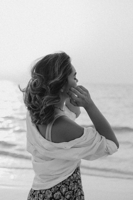 A contemplative woman gazes at the calming sea in a black and white setting.