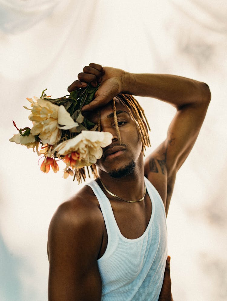 A Man In A White Tank Top Holding Flowers 