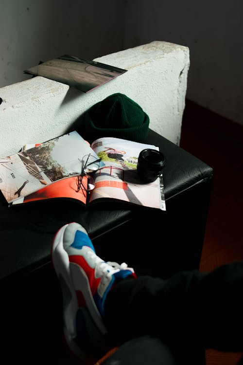 Free From above of crop unrecognizable male in stylish sneakers sitting near opened magazine with pictures Stock Photo