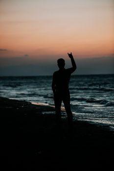 Silhouette of a man making a hand gesture at sunset on a beach. Captured in serene dusk ambiance.