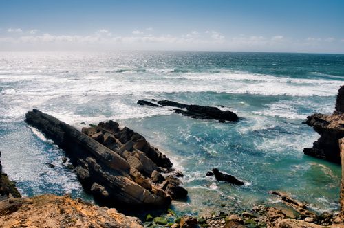 Free Breathtaking view of a rocky shoreline with crashing waves under a clear blue sky. Stock Photo