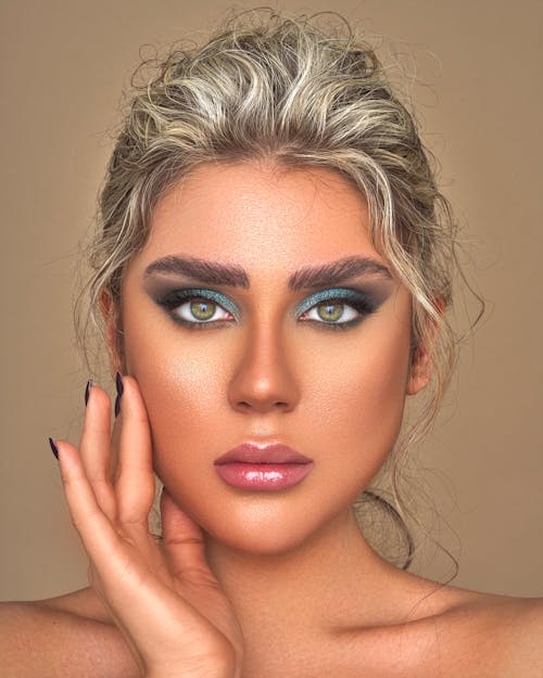 Free Attractive blond lady with bright makeup and bare shoulders looking at camera against brown background Stock Photo