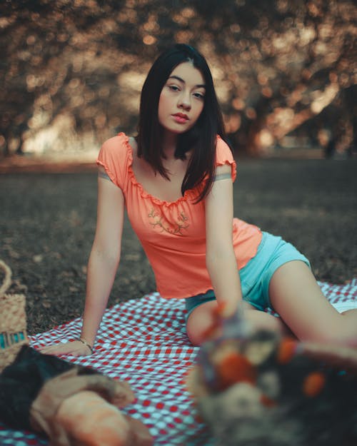 A Woman in Orange Shirt Sitting on the Blanket