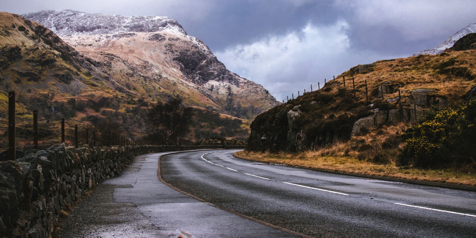 A curving road leading through mountainous countryside under cloudy skies