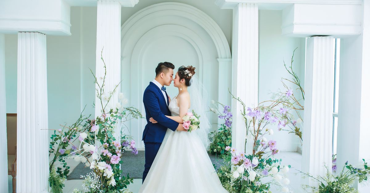 A romantic moment captured between a bride in a wedding gown and groom in formal attire, surrounded by beautiful floral arrangements.