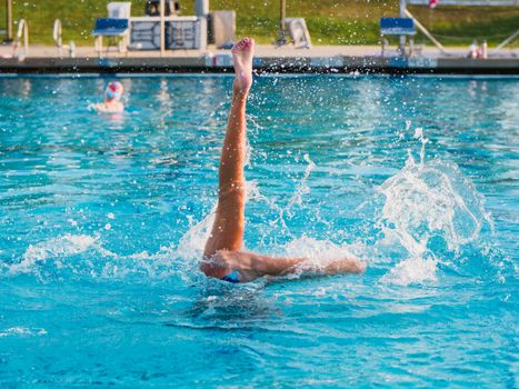 Dynamic shot of a synchronized swimmer performing an artistic leg move in a pool.