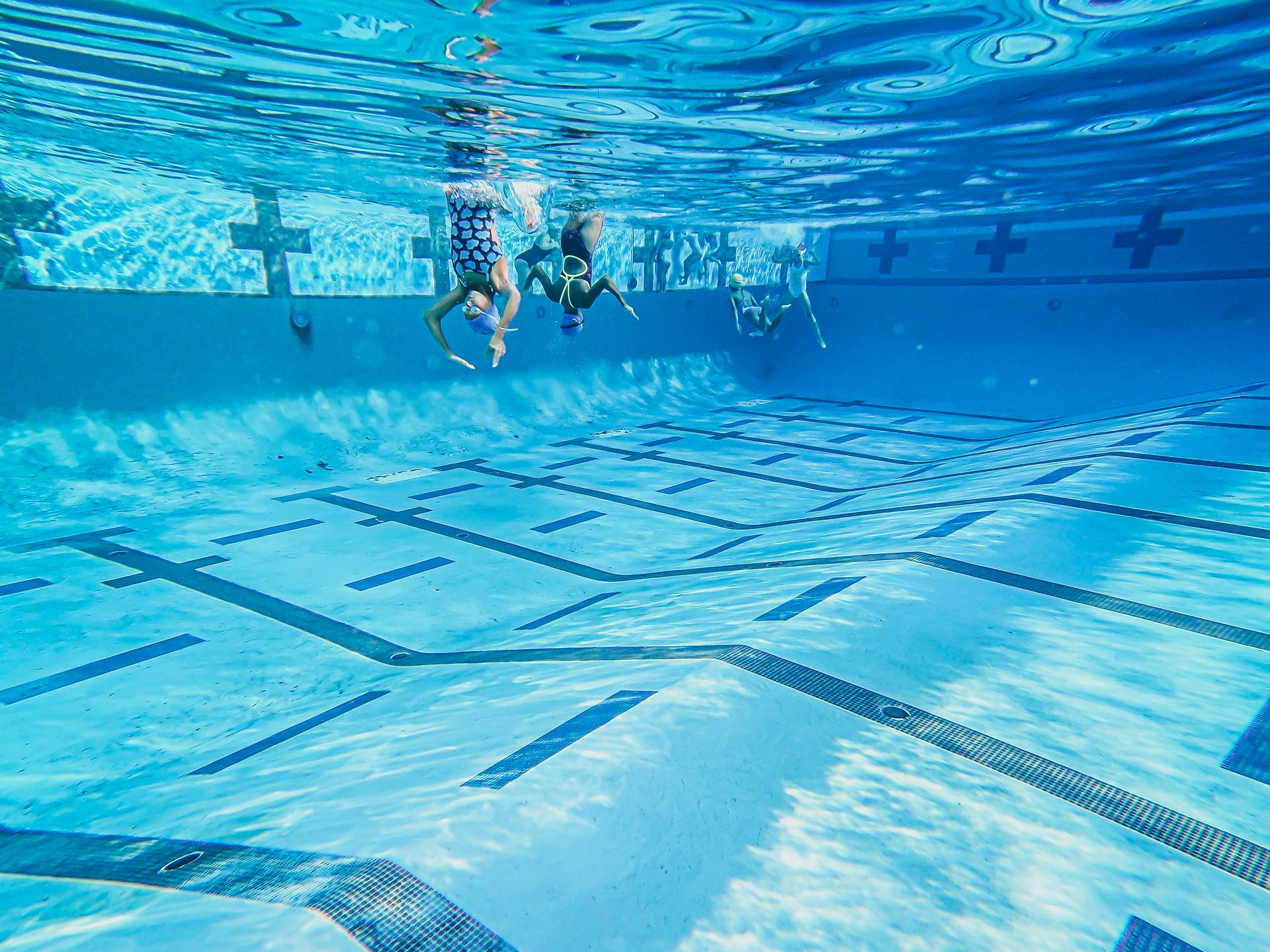 Young swimmers enjoy diving in a crystal-clear swimming pool.